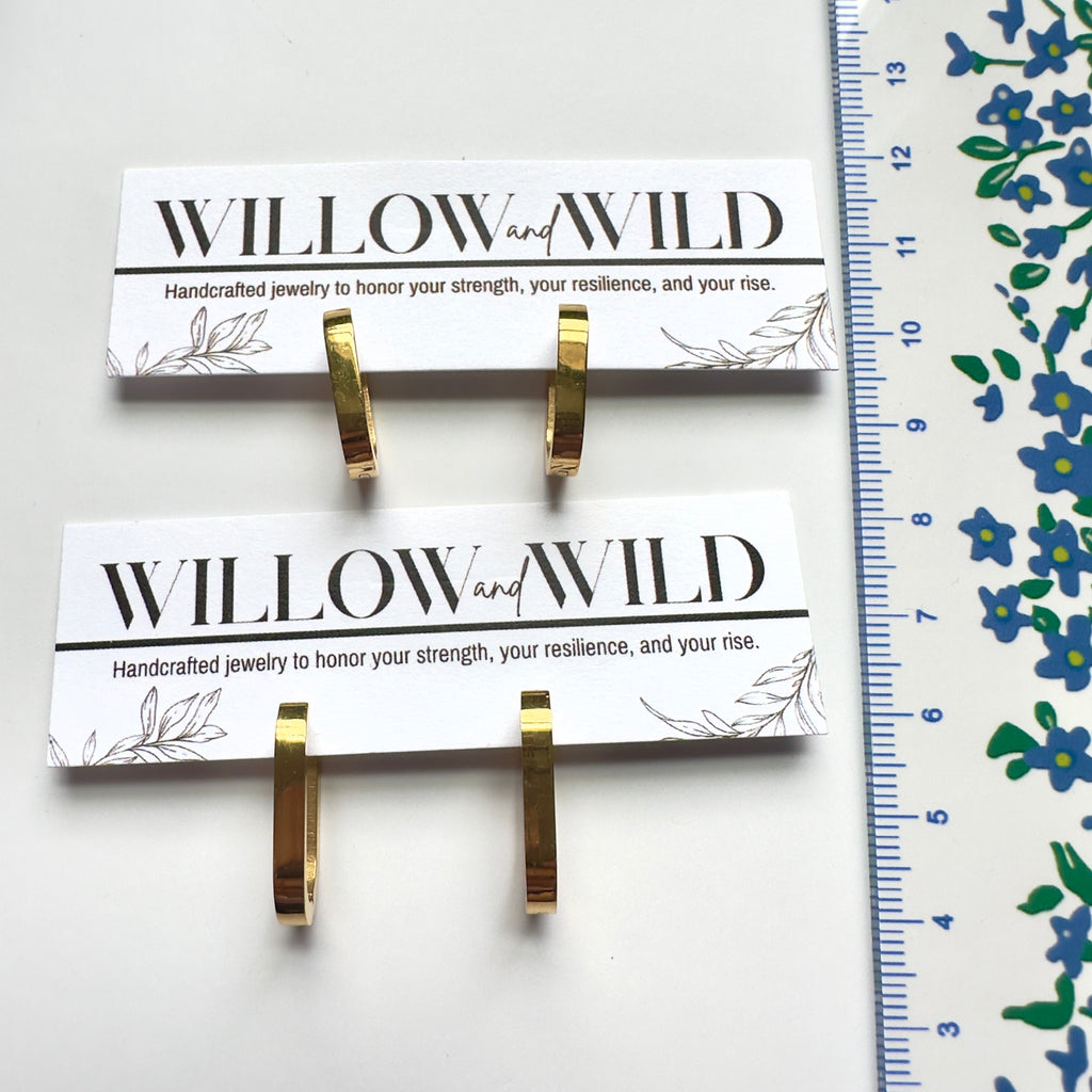 Two gold hoop earrings displayed on white branded jewelry cards, with a blue-and-white ruler along the right side for scale. The cards read WILLOW and WILD.