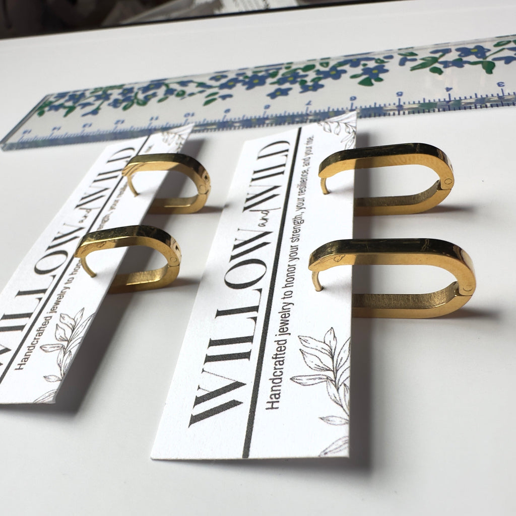 Four gold-toned metal ring stands with printed white cards, arranged on a white surface with a floral ruler in the background.